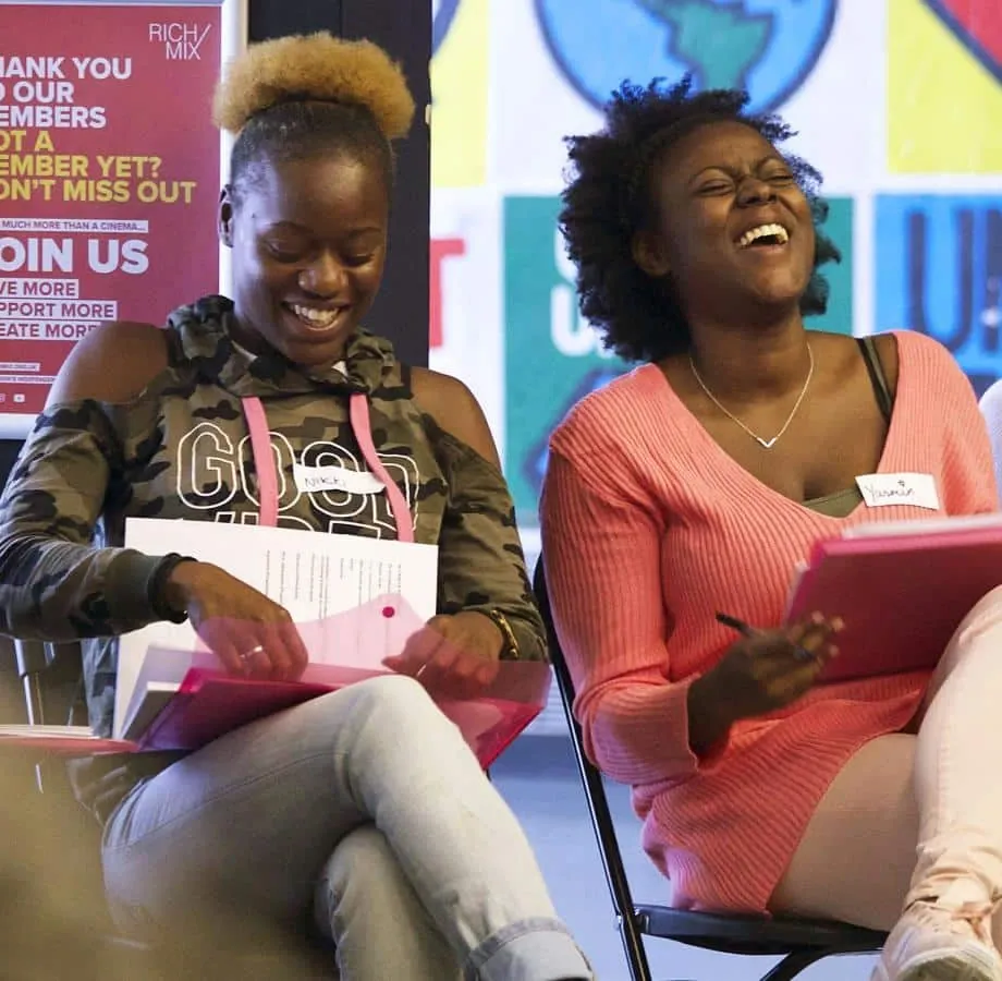 Two women smiling and laughing with notebooks during a workshop.