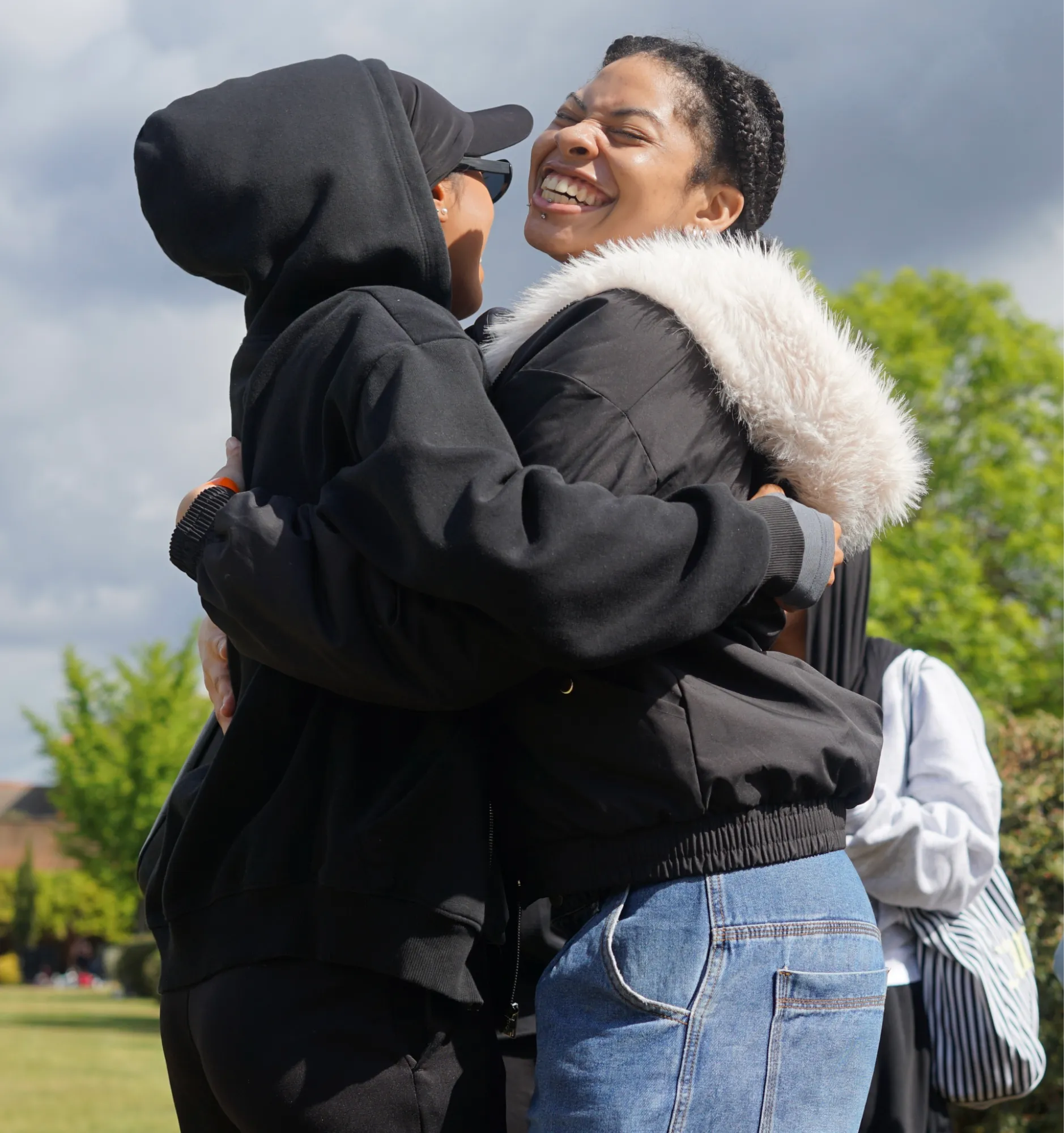 Two people embracing outdoors on a grass field, one smiling broadly.