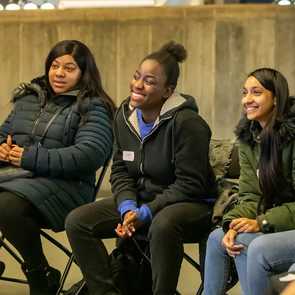 Three women seated together, smiling and listening during a group gathering.