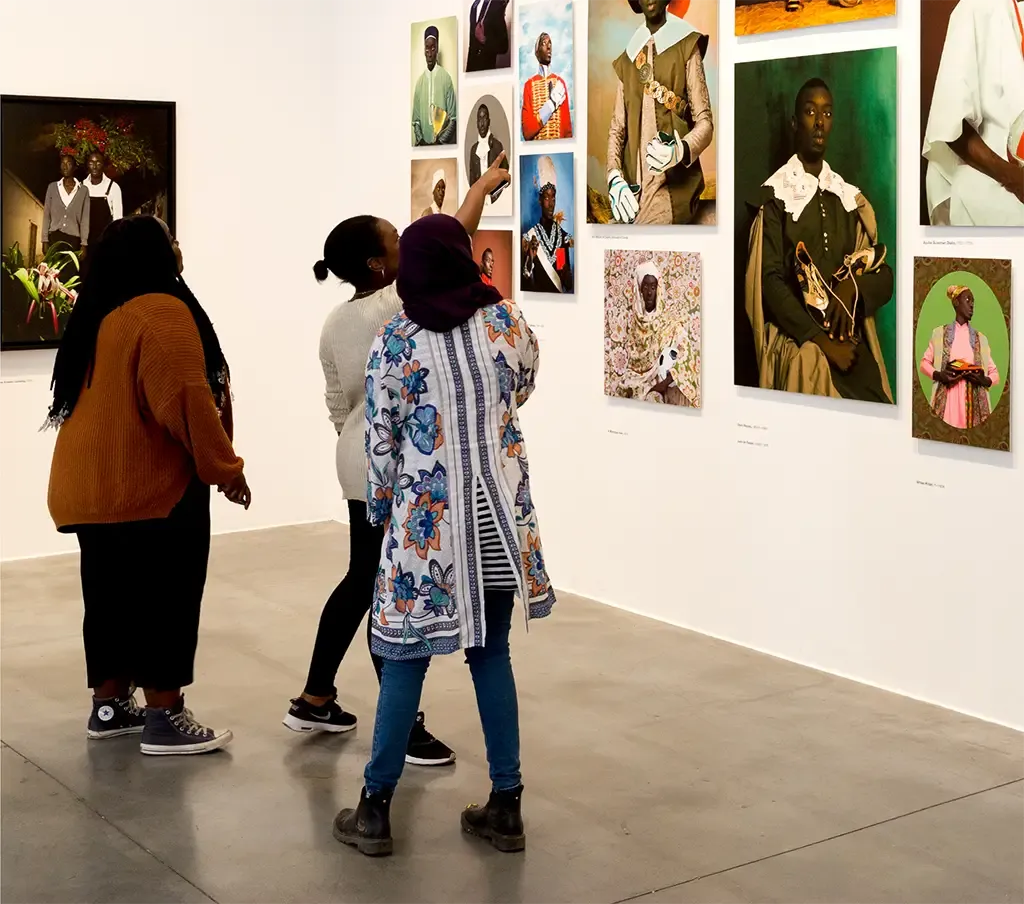 Three people looking at photographic portraits on the walls of an art gallery.