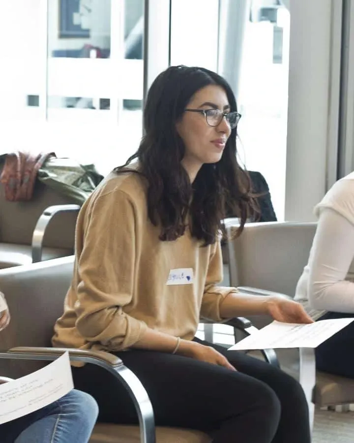 A woman with glasses seated with papers during a group discussion.