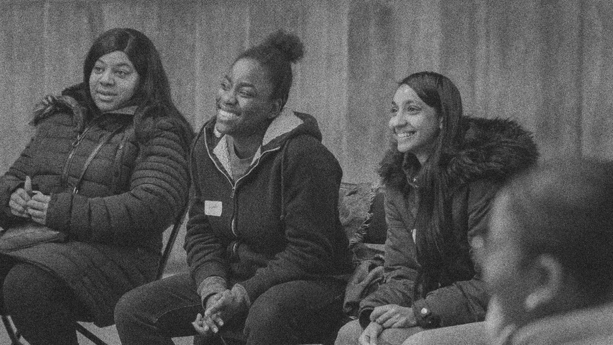 Three women seated together, listening to someone in front of them.