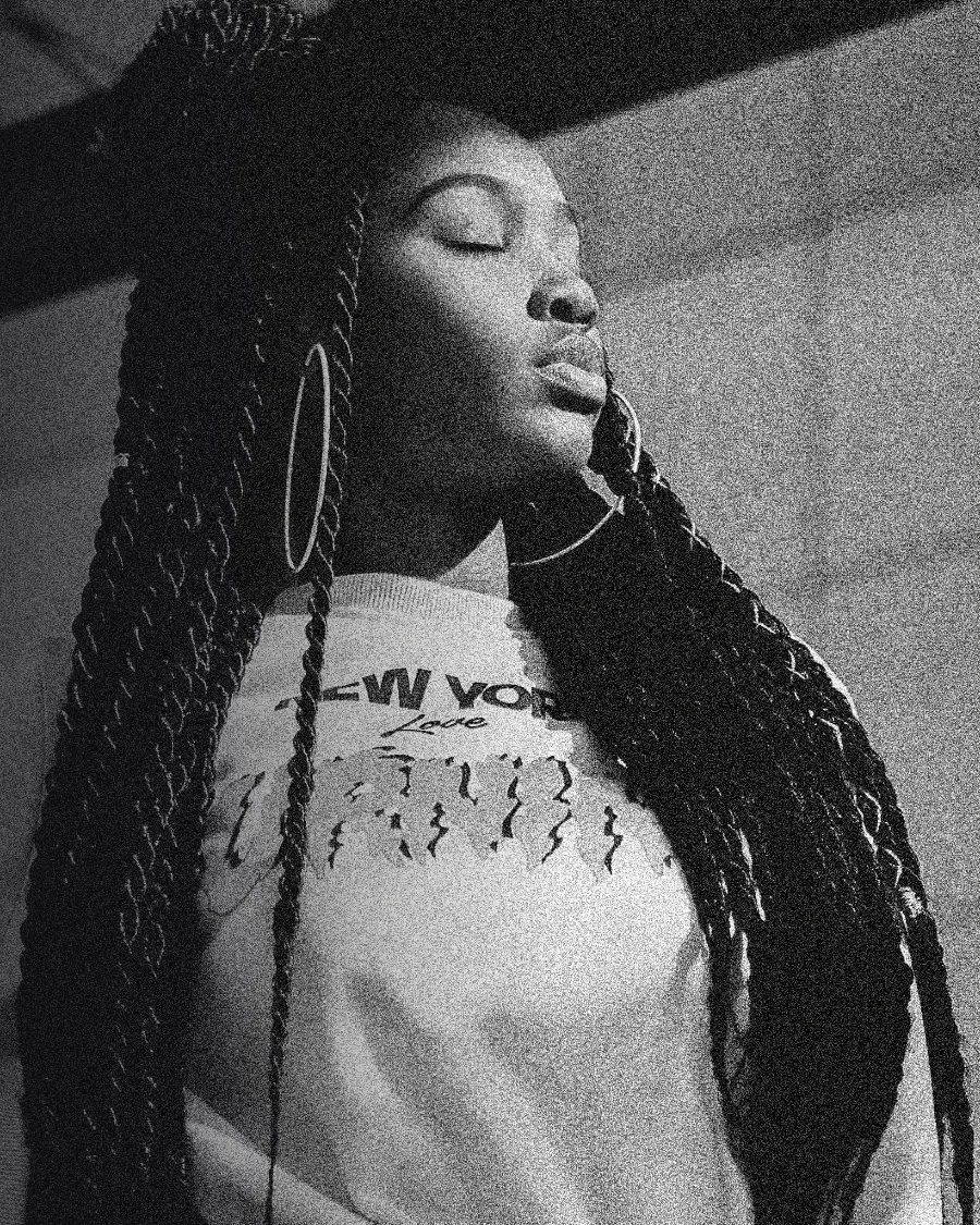 A woman with long braids moving with her eyes closed in a studio.
